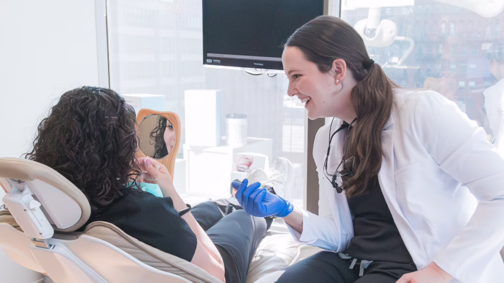 Dentist in a white coat smiling while examining a patient in a dental chair.
